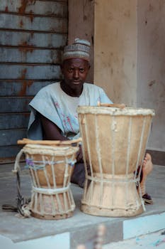 Man with traditional drums in a rustic outdoor setting, promoting cultural heritage.